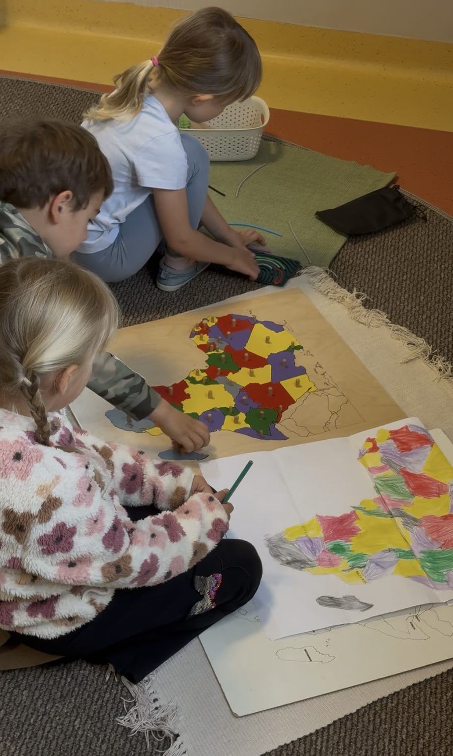 Dzieci pracujące z mapą Montessori na dywanie